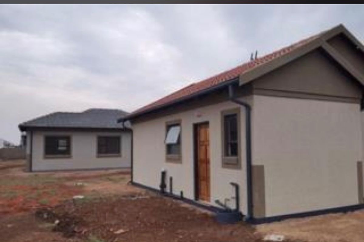 Rear view of a newly constructed residential house featuring a tiled roof, exterior plumbing, and unlandscaped surrounding grounds.