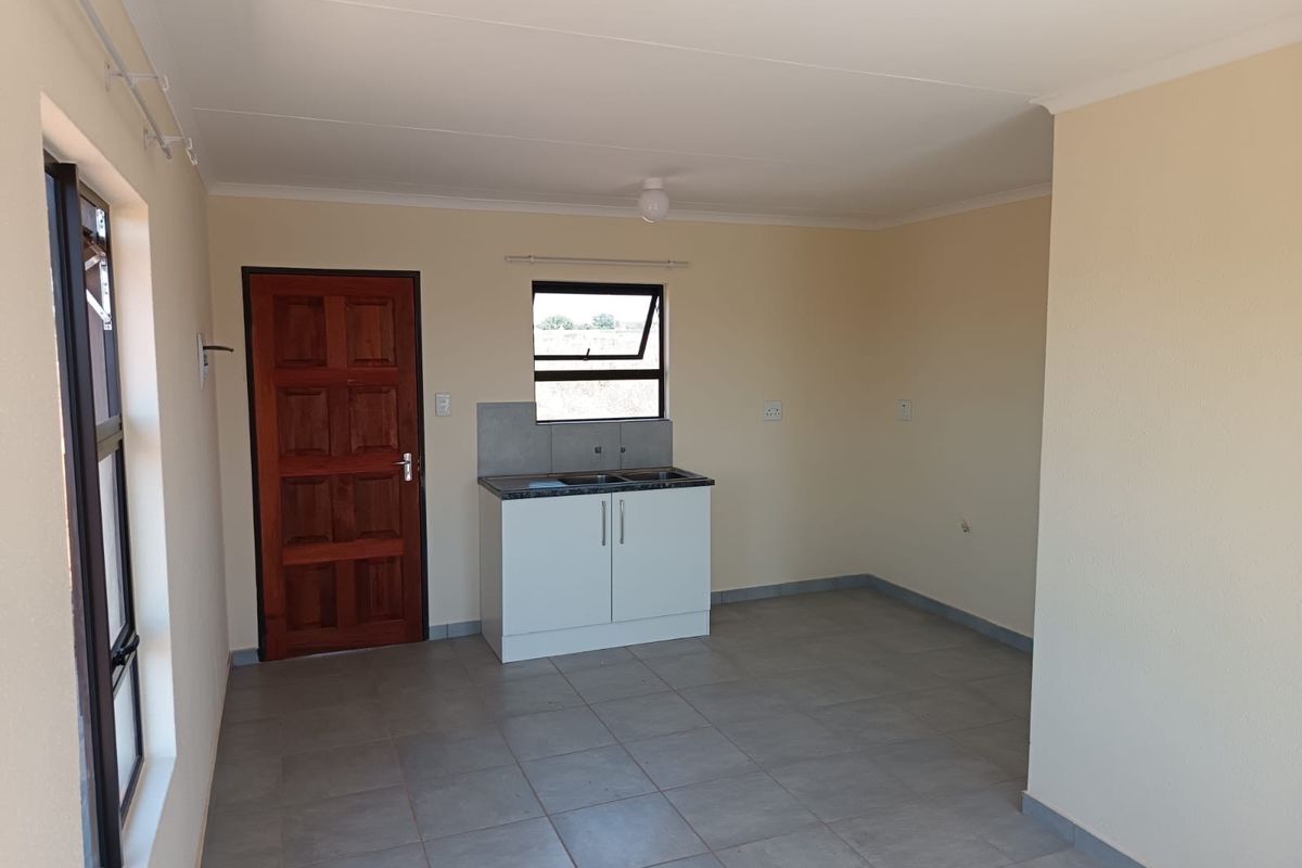 A compact, empty kitchen area featuring tiled flooring, a small base cabinet with a sink, and neutral wall finishes.