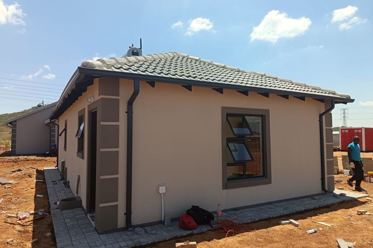 Rear view of a modern single-story house featuring a tiled roof, aluminium window frames, and a paved walkway surrounding the structure.