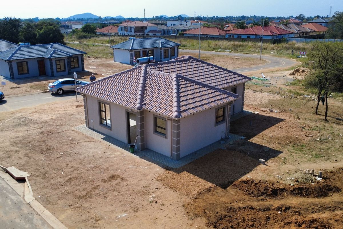 Aerial view of a newly constructed residential house featuring a tiled roof, solar geyser, and surrounding unlandscaped plot in a developing estate.