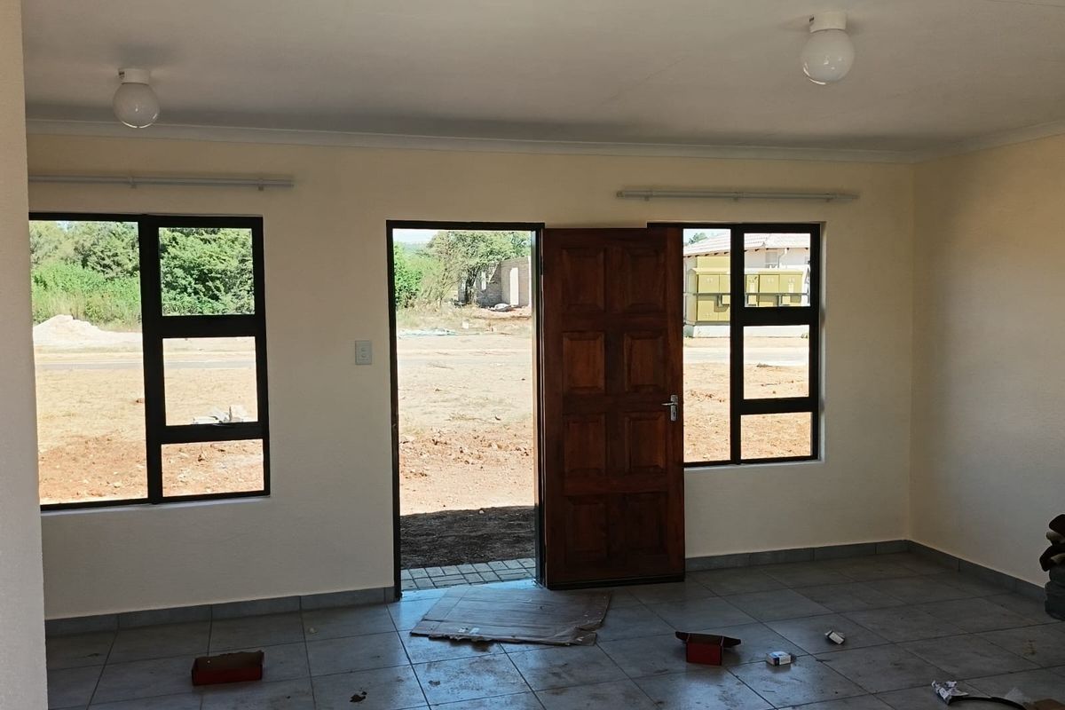 An empty living room featuring tiled flooring, aluminium window frames, and a timber entrance door, offering a blank canvas for interior design.