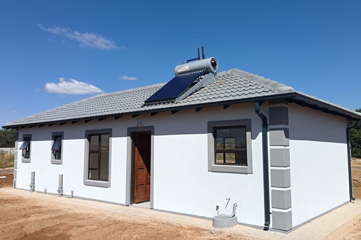 Rear view of a modern single-story house featuring a tiled roof, solar water heating system, and clean exterior finishes with surrounding unlandscaped ground.