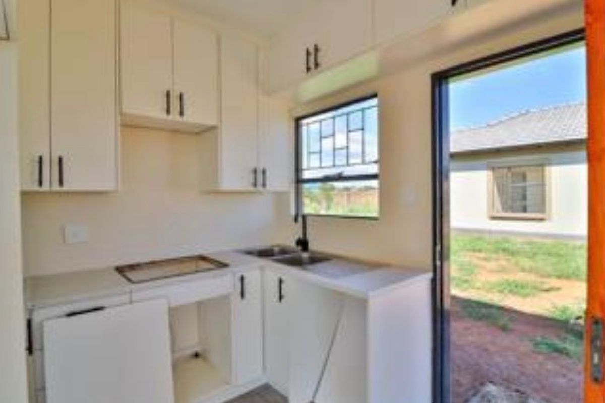 A compact kitchen area featuring white cabinetry, a stainless steel sink, and direct access to the rear yard through a sliding door.