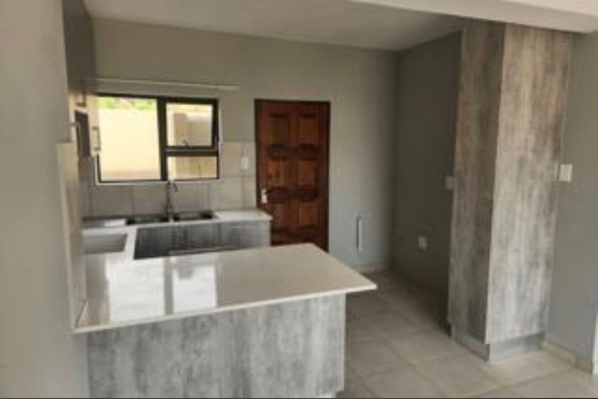 A modern kitchen featuring grey wood-look cabinetry, stone countertops, a double bowl sink, and tiled flooring in an open-plan layout.