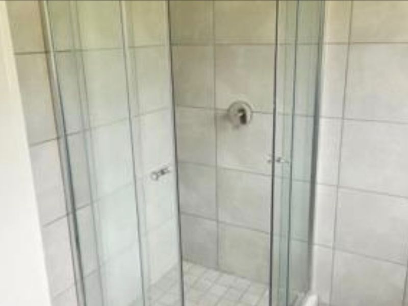 A clean, functional bathroom shower enclosure featuring modern glass panels and neutral ceramic wall tiling.