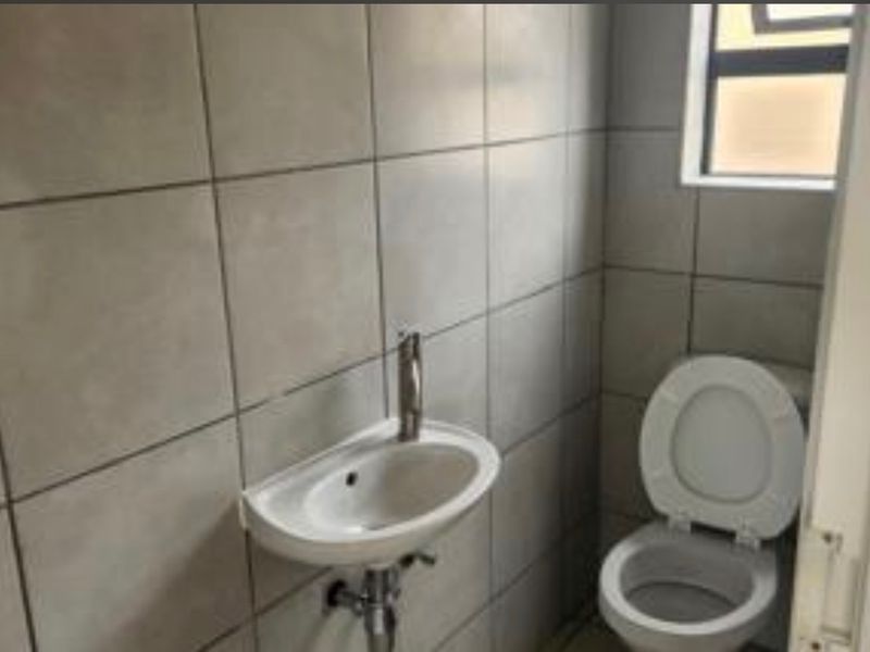A compact guest bathroom featuring tiled walls, a wall-mounted basin, and a standard toilet.