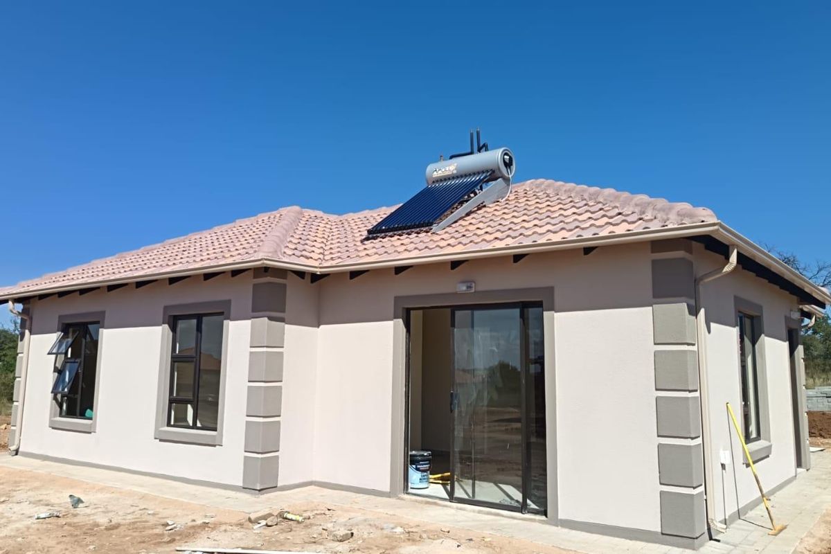 Rear view of a modern single-story house featuring a tiled roof, solar water heating system, and sliding glass door access.