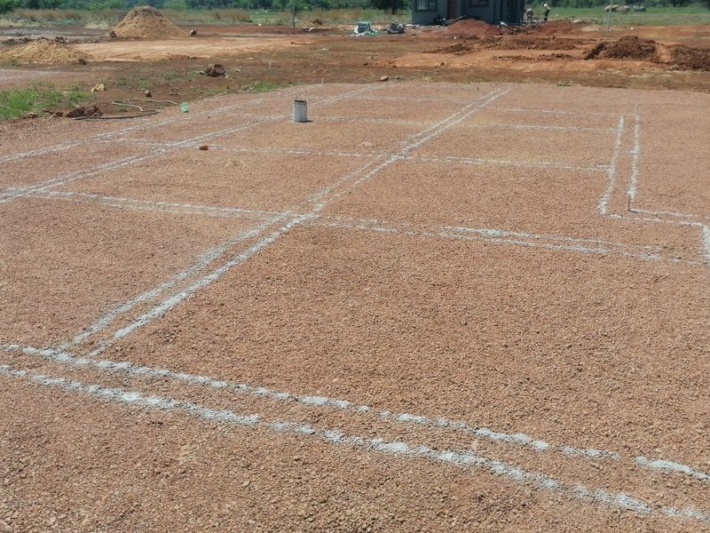 A vacant plot of land showing the initial foundation layout markings and plumbing pipe stubs for a new residential construction project.