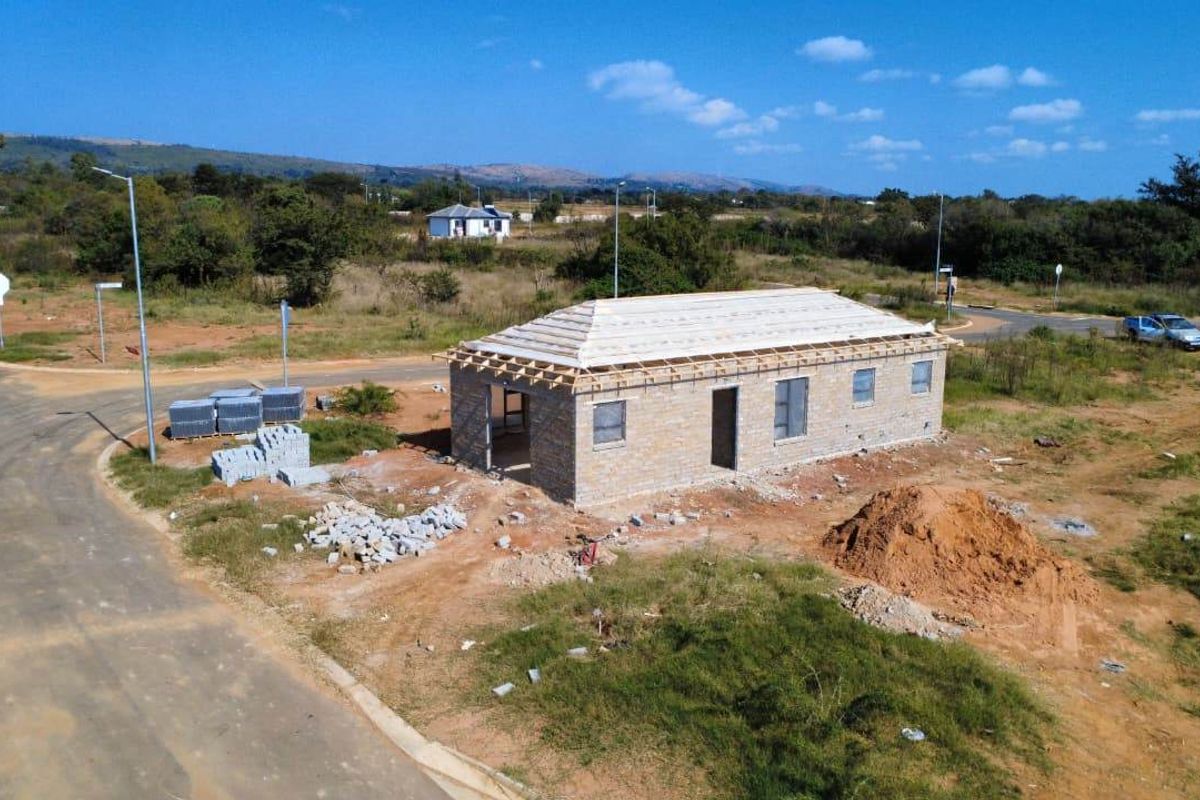 Aerial view of a residential property currently under construction, featuring brick walls and timber roof trusses on a large corner plot.