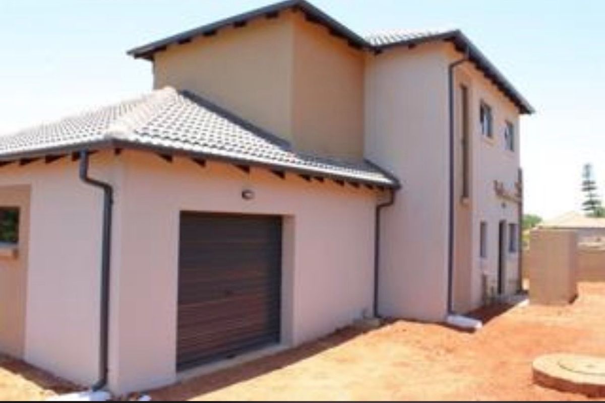 Rear view of a two-story residential property featuring a garage, tiled roof, and plastered exterior walls, currently set on an unfinished plot.