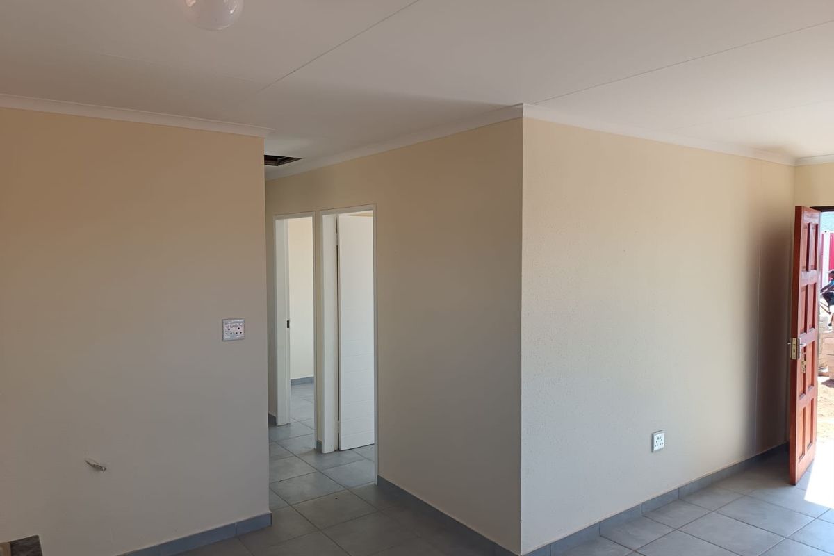An empty, neutrally painted living area featuring tiled flooring, coving, and access to adjacent rooms through internal doorways.