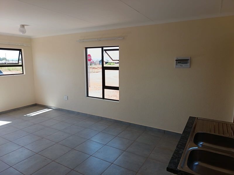 An open-plan living and kitchen area featuring tiled flooring, neutral walls, and a built-in stainless steel sink unit.