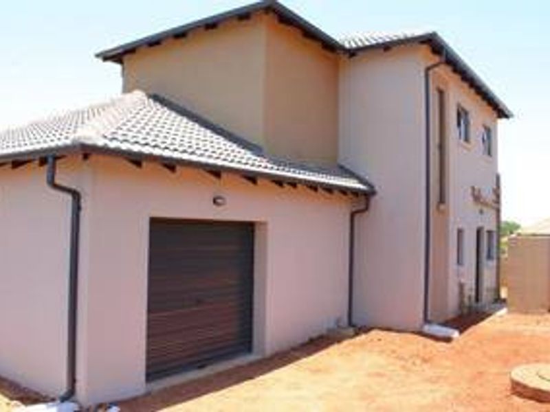 Rear view of a double-story residential house featuring a single garage, tiled roof, and plastered exterior walls with unfinished surrounding ground.