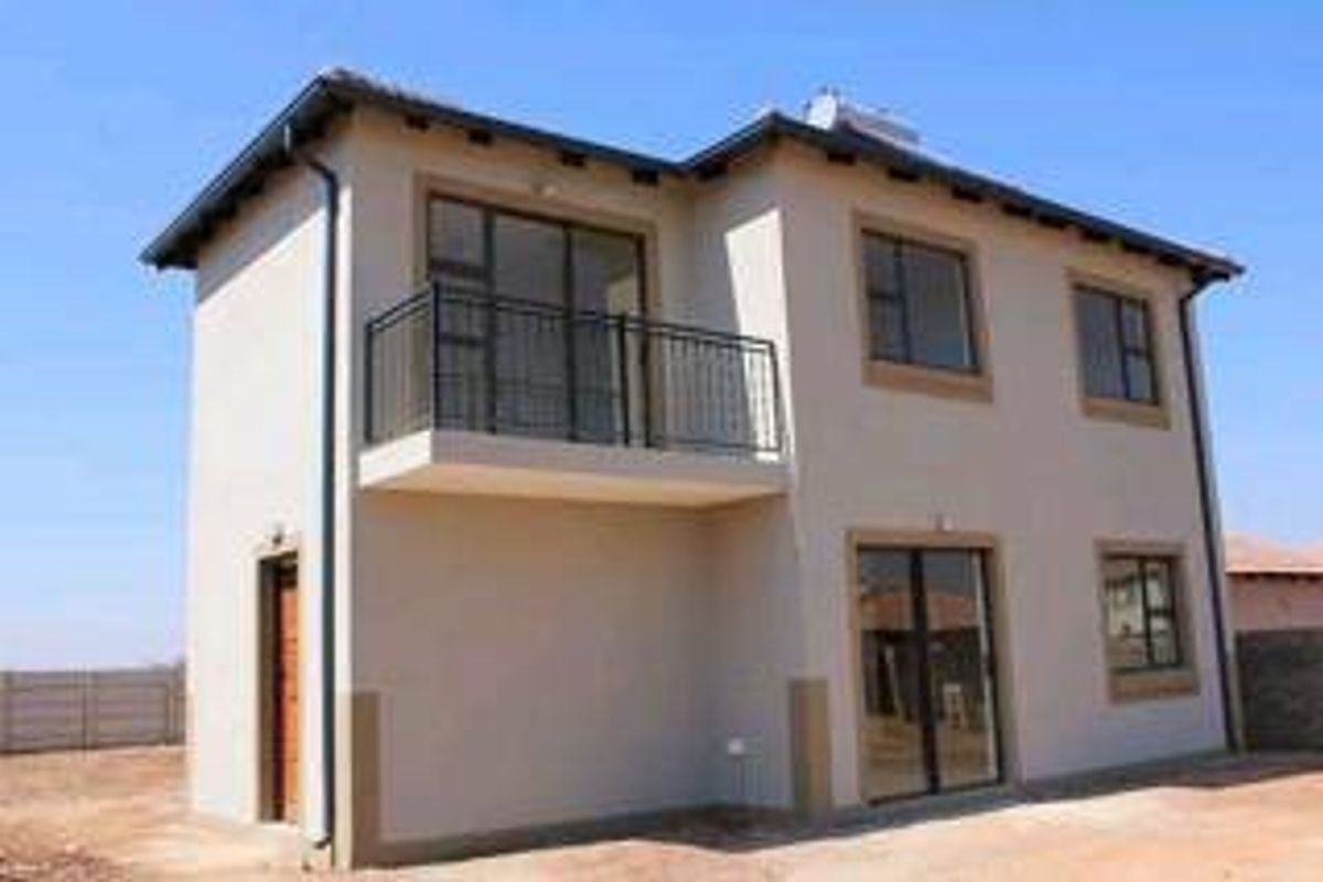 A modern double-story house exterior featuring a balcony with metal railings, sliding glass doors, and a solar water heating system on the roof.
