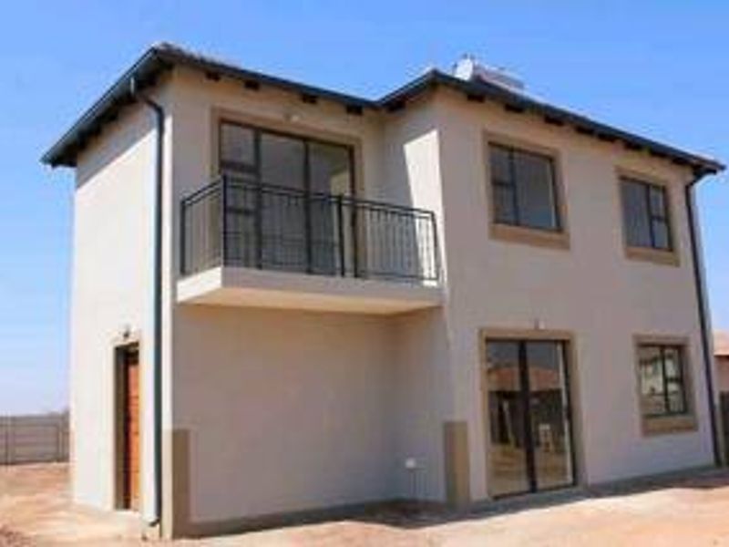 A modern double-story house exterior featuring a balcony with metal railings, sliding glass doors, and a solar water heating system on the roof.