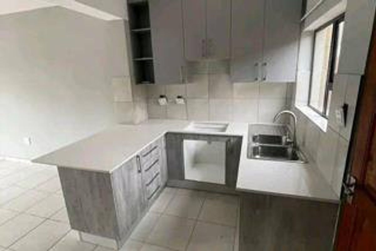 A clean, modern kitchen featuring grey cabinetry, stone countertops, a double bowl sink, and tiled flooring, presented in a vacant, move-in ready condition.