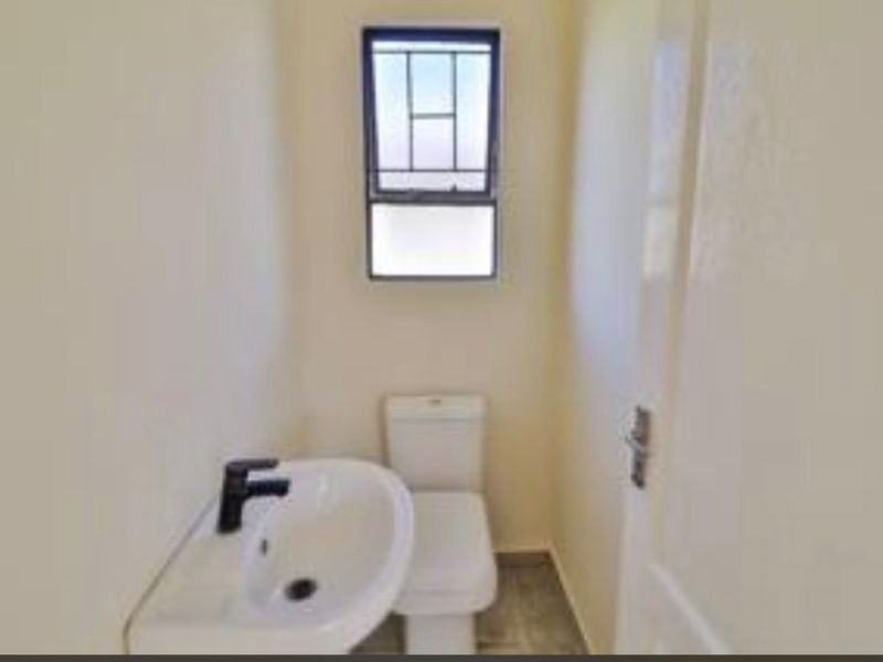 A compact, clean guest bathroom featuring a modern white toilet, pedestal washbasin with a black faucet, and a window for natural light.