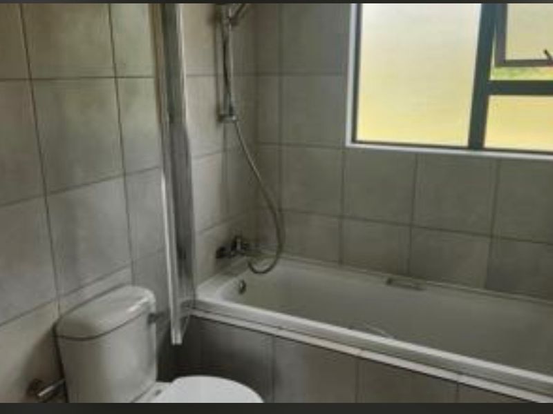 A functional bathroom featuring a bathtub with shower attachment, toilet, and tiled wall finishes, requiring cosmetic updates to improve its overall condition.