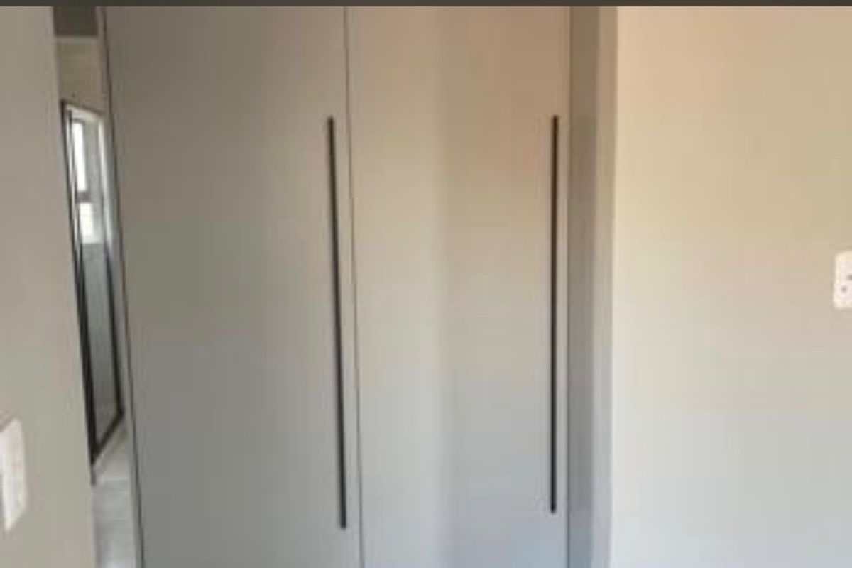 A bedroom interior featuring modern built-in cupboards with sleek vertical handles.