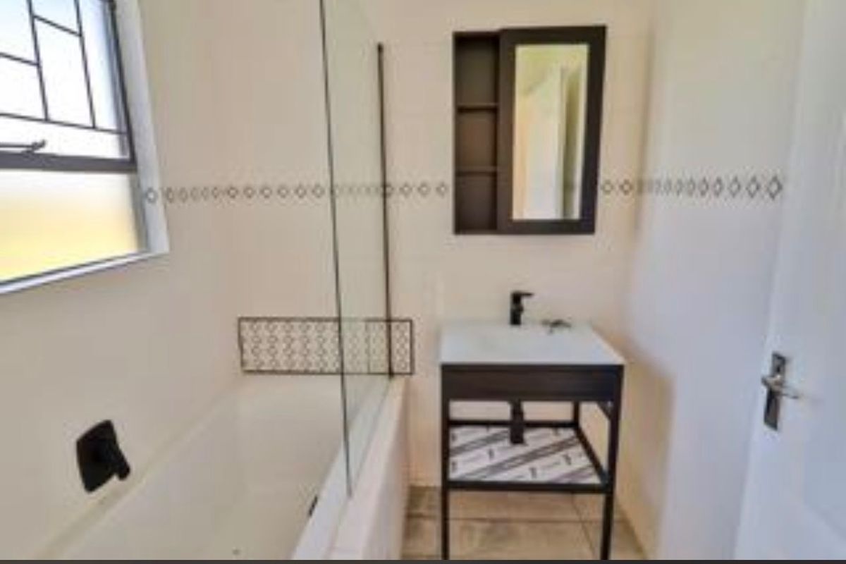 A clean, modern bathroom featuring a bathtub with a glass screen, a contemporary vanity unit, and a wall-mounted medicine cabinet.