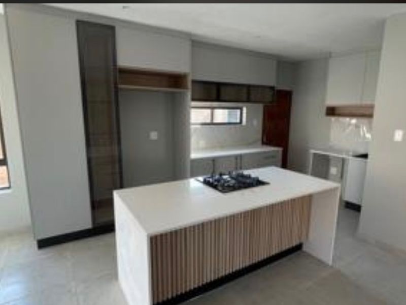 Modern kitchen featuring a central island with a gas hob, stone countertops, and contemporary cabinetry with slatted wood detailing.