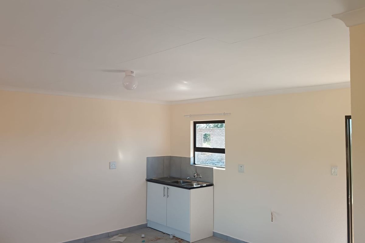 A compact, empty kitchen area featuring a single base cabinet unit with a sink, tiled splashback, and neutral wall finishes.