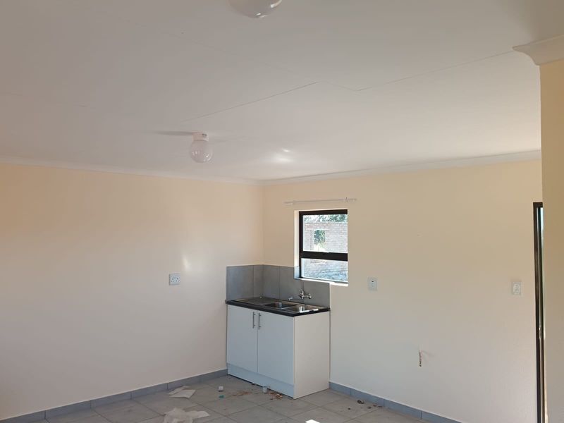 A compact, empty kitchen area featuring a single base cabinet unit with a sink, tiled splashback, and neutral wall finishes.