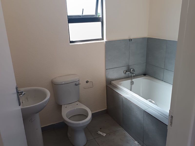 A functional bathroom featuring a pedestal basin, toilet, and a tiled bathtub area with a top-hung window for natural light.