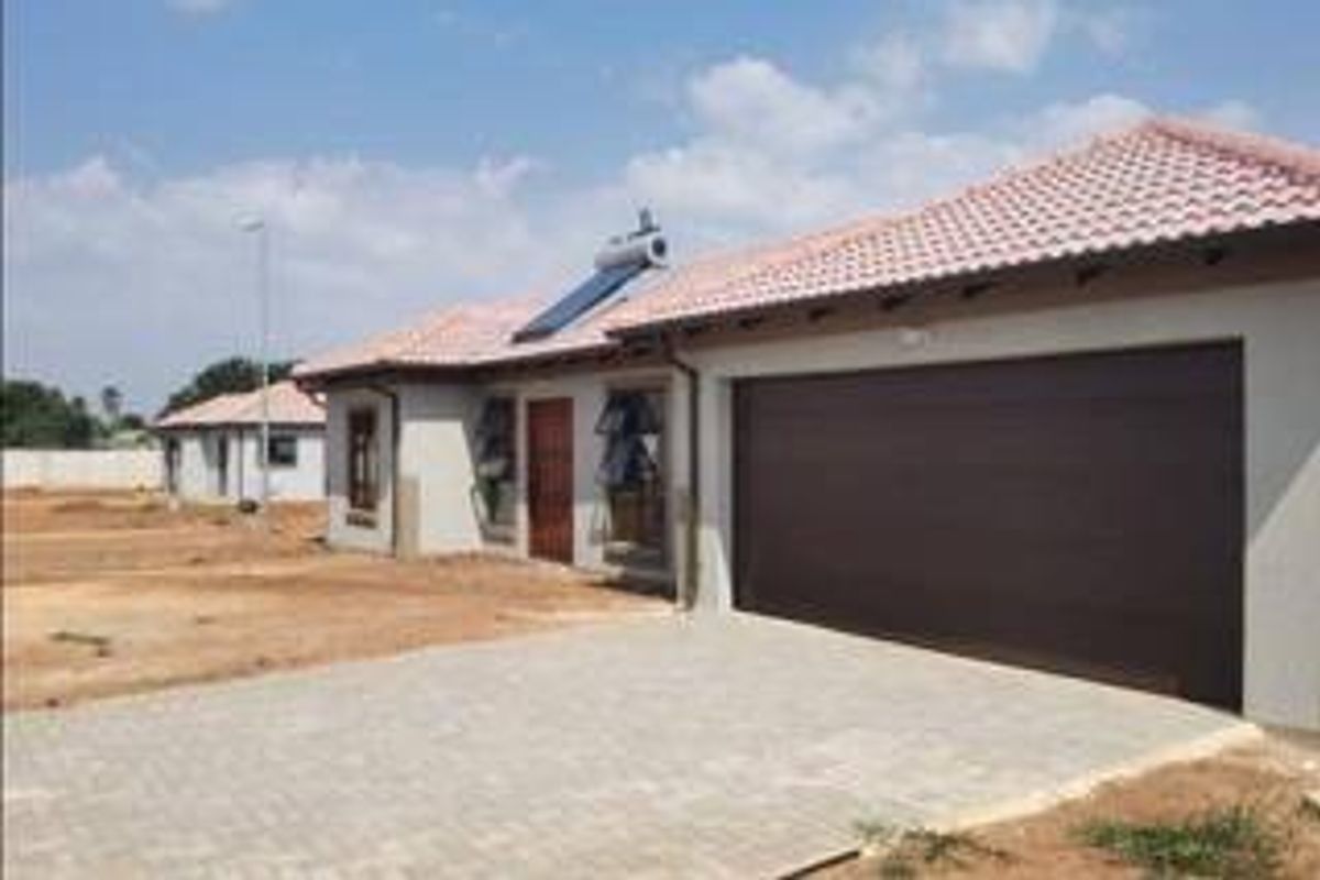 Front view of a modern single-story house featuring a paved driveway, integrated garage, and a solar geyser installed on the tiled roof.