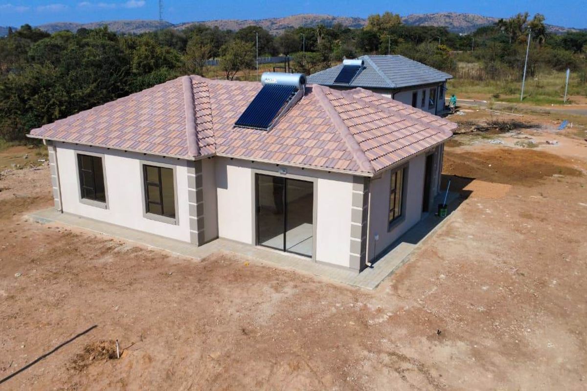 Aerial view of a modern single-story house featuring a tiled roof with a solar water heater and surrounding unlandscaped grounds.