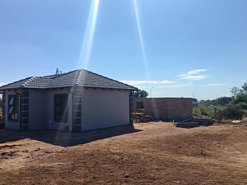 Rear view of a modern house with tiled roof and aluminium windows, set on a large, undeveloped plot of land.