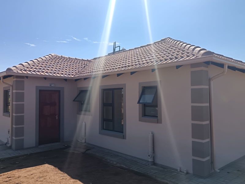A well-maintained rear exterior view of the house featuring a tiled roof, modern aluminium window frames, and a paved walkway.
