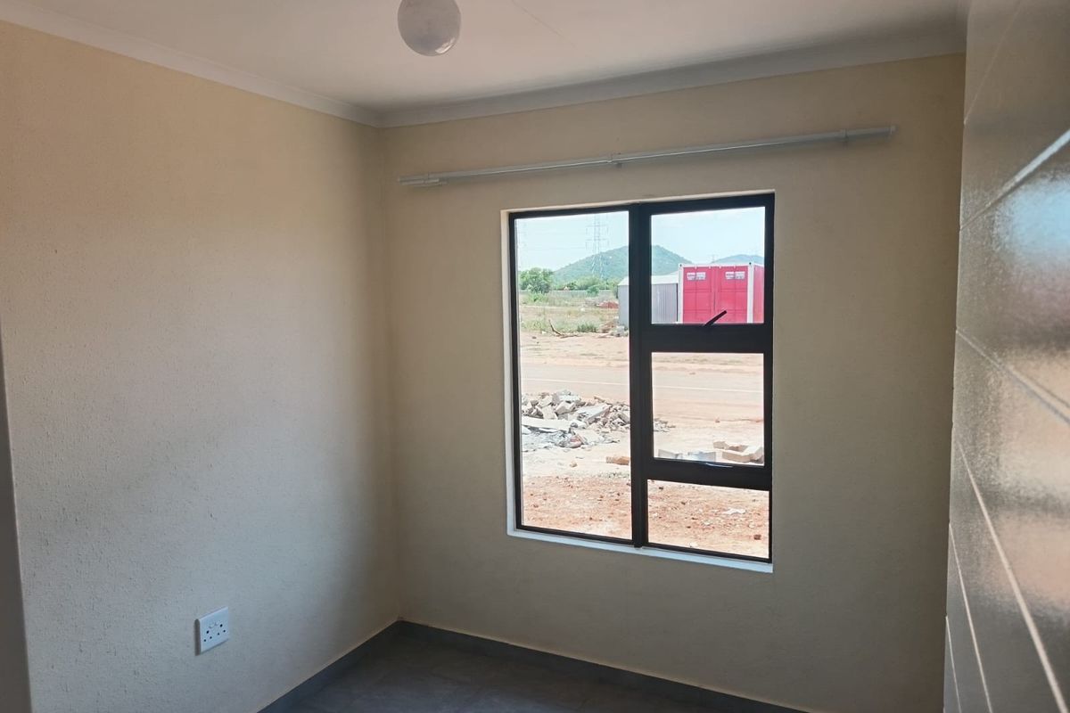 A clean, empty bedroom featuring tiled flooring, neutral walls, and an aluminium-framed window with a curtain rail.