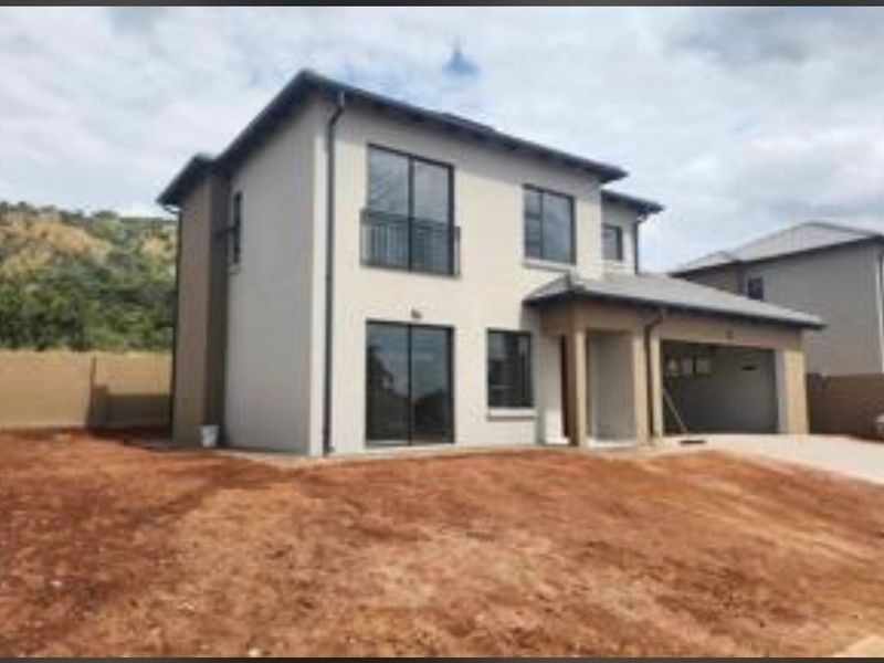 Modern double-storey residential property featuring an integrated garage, balcony, and large sliding glass doors, set on a plot with an unlandscaped garden.