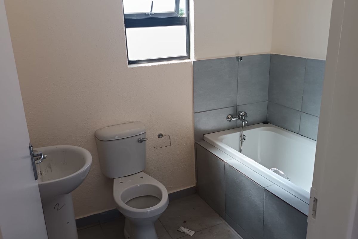 A functional bathroom featuring a pedestal basin, toilet, and a tiled bathtub surround with a top-hung window for natural light.