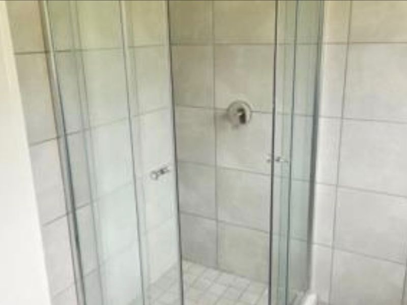 A functional bathroom shower enclosure featuring glass doors and neutral ceramic wall tiling.