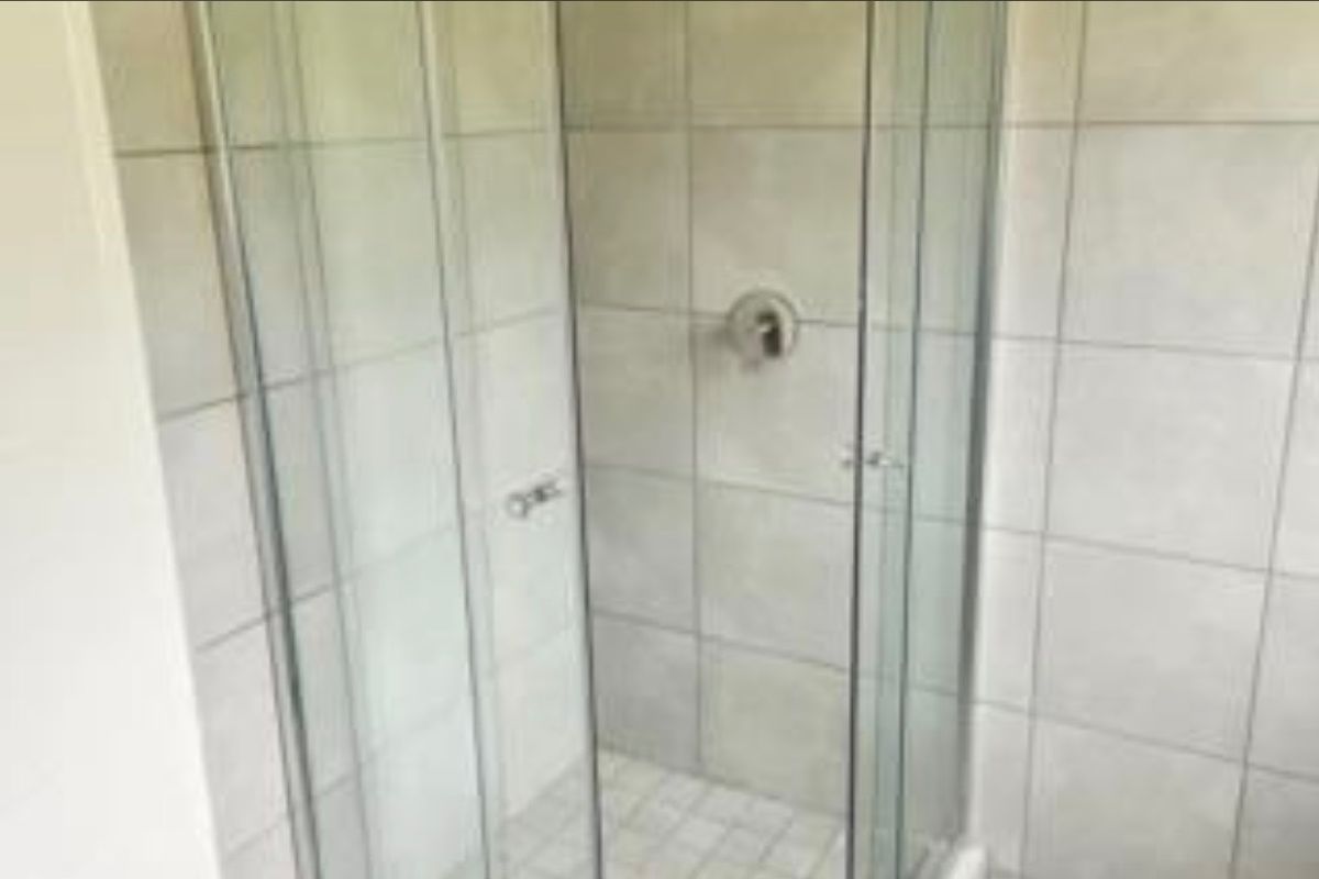 A functional bathroom shower enclosure featuring glass doors and neutral ceramic wall tiling.