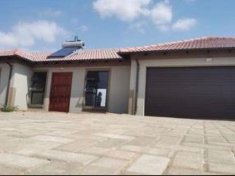 Front elevation of a modern single-story house featuring a paved driveway, integrated garage, and roof-mounted solar water heating system.