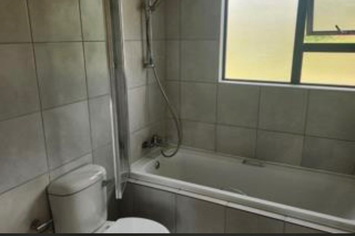 A functional bathroom featuring a bathtub with a shower mixer, toilet, and tiled wall finishes, requiring some cosmetic updates.