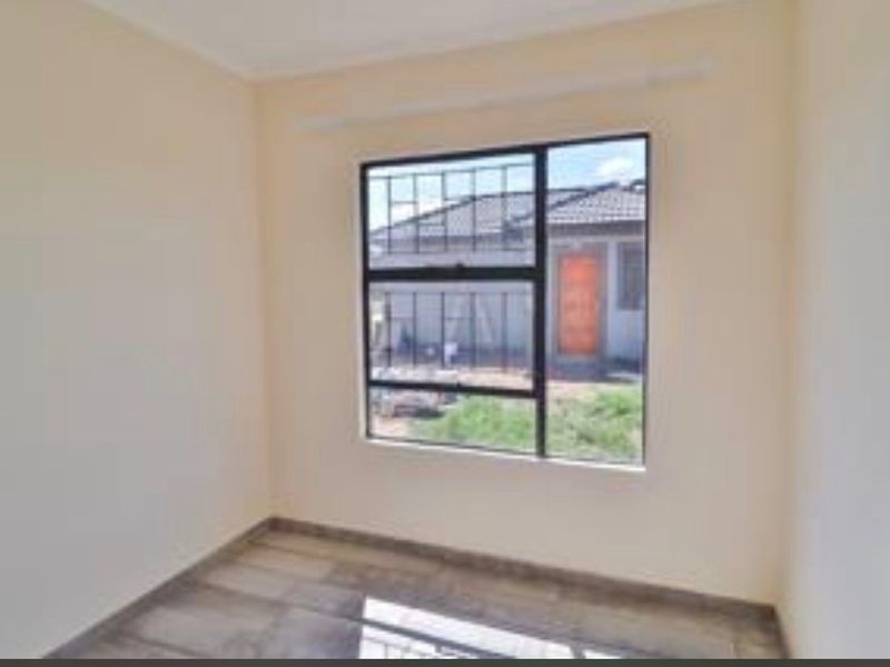 A bright, empty bedroom featuring tiled flooring and a window fitted with security bars, offering a clean and neutral space.