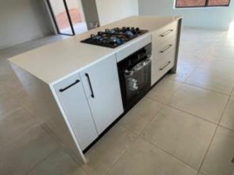A modern kitchen island featuring a built-in gas hob, oven, and stone countertop, set within a spacious, tiled open-plan living area.