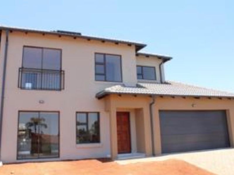 A modern double-storey residential home featuring a tiled roof, integrated double garage, and a balcony, set on a paved driveway.