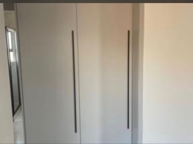A bedroom interior featuring modern built-in cupboards with sleek vertical handles.
