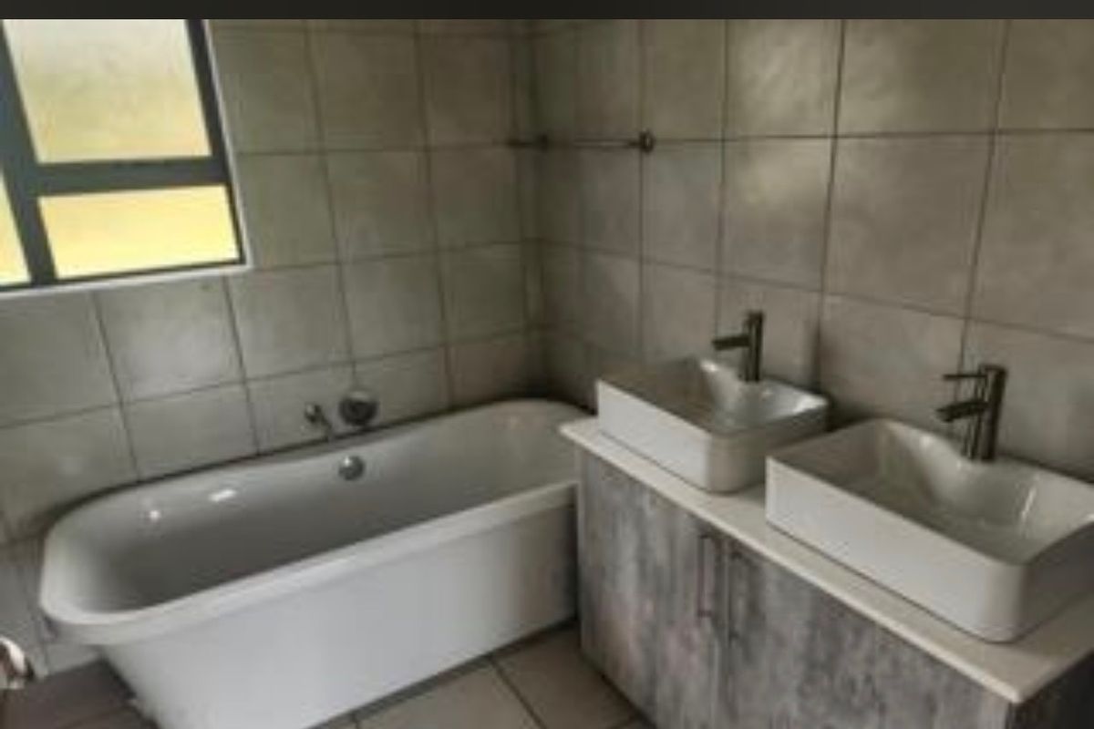 A modern bathroom featuring a freestanding bathtub and a double vanity with vessel sinks, finished with neutral wall and floor tiling.