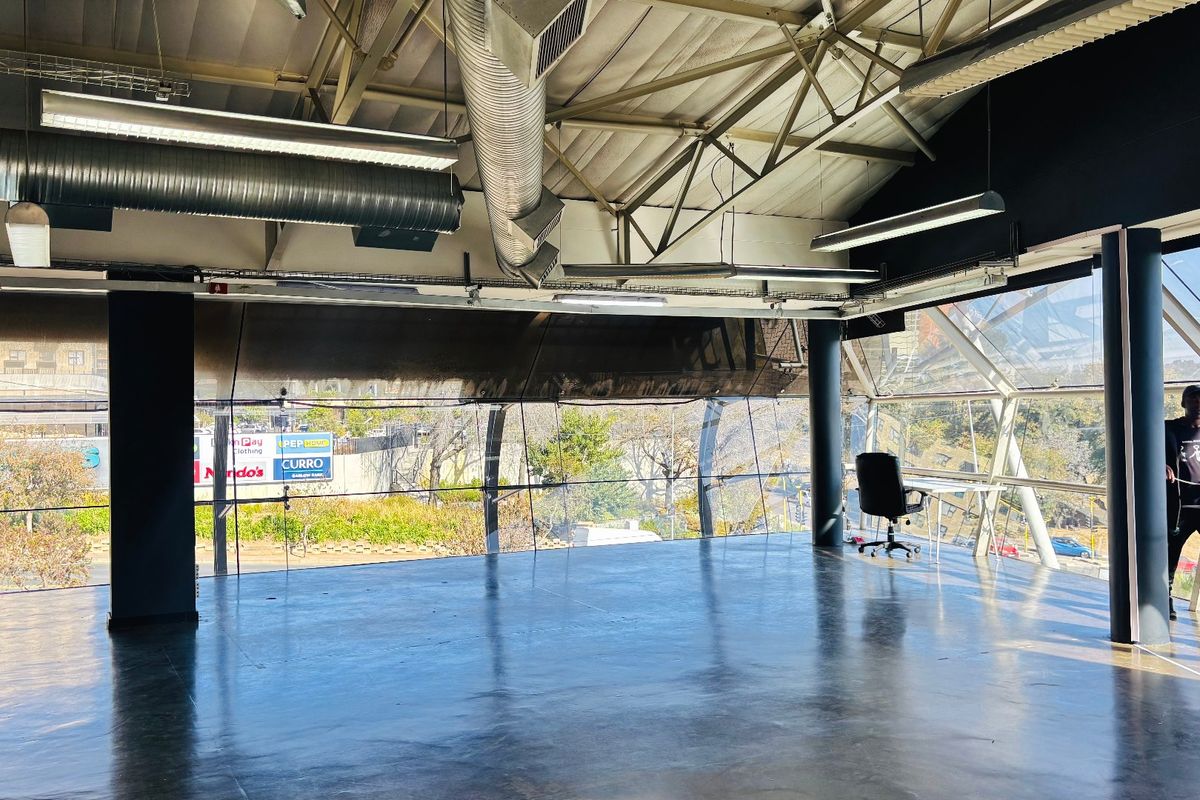 Spacious open-plan commercial office space featuring polished concrete floors, exposed industrial ceiling elements, and expansive glass walls providing ample natural light.