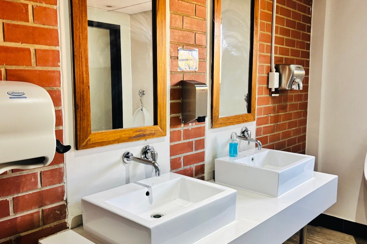 Commercial bathroom featuring a double vanity with wall-mounted faucets, exposed brick wall finish, and a wall-mounted urinal.