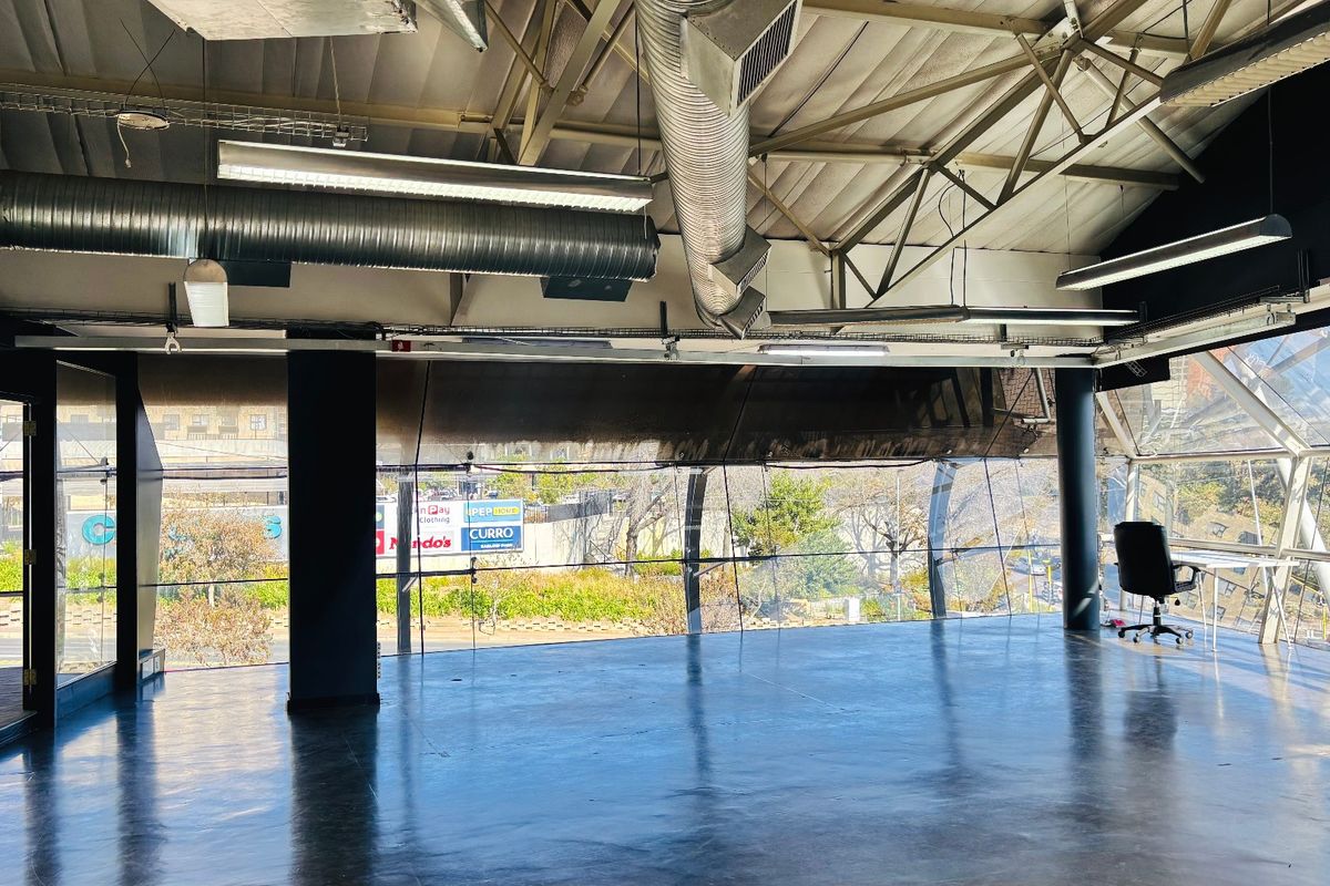 Spacious open-plan commercial office space featuring industrial-style exposed ceilings, polished concrete floors, and expansive glass walls offering significant natural light.