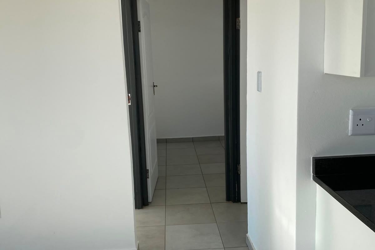A clean, neutral hallway featuring tiled flooring and a ceiling access hatch, providing a bright and functional transition space between rooms.