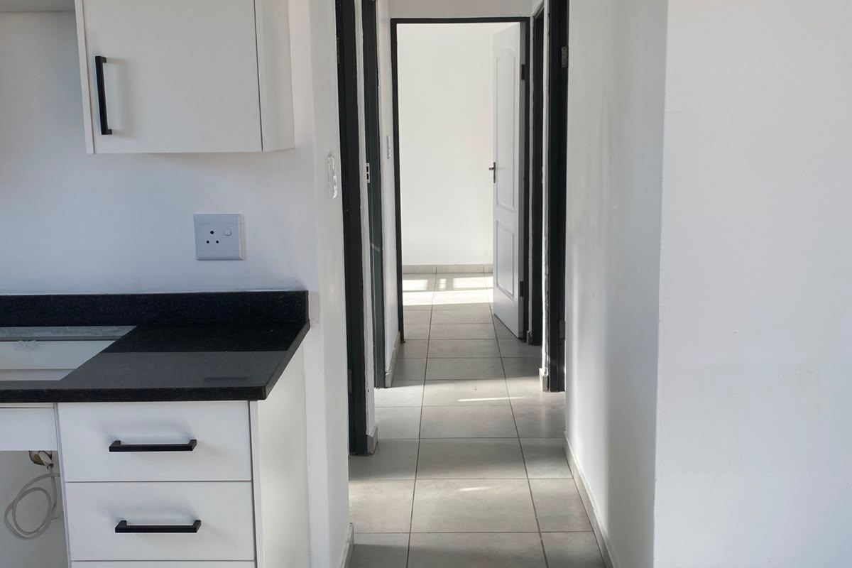 A clean, modern kitchen area featuring white cabinetry, dark stone countertops, and tiled flooring, leading into a hallway with multiple doorways.
