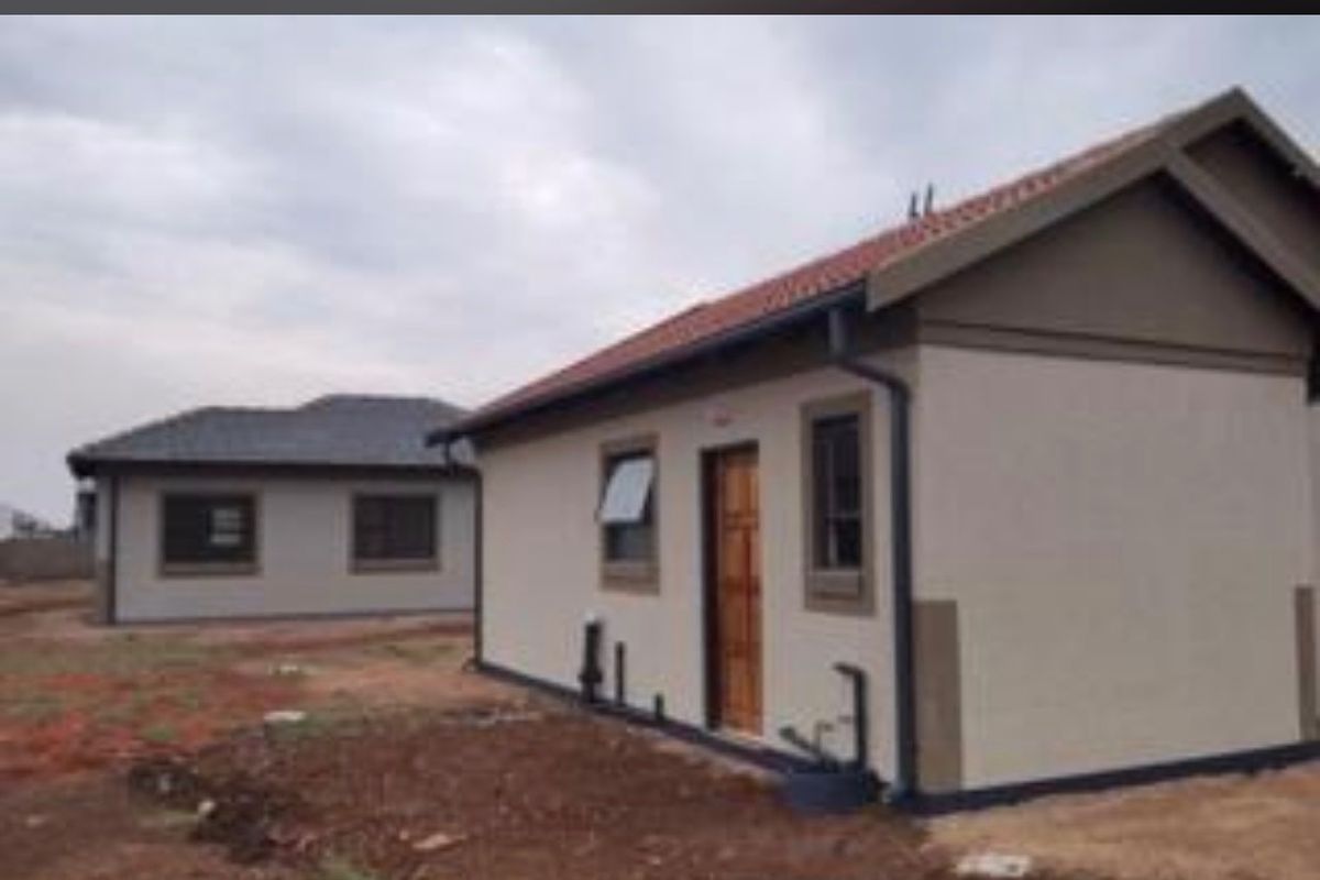 A view of the rear exterior of a modern residential house featuring a tiled roof, neutral exterior walls, and installed gutters.